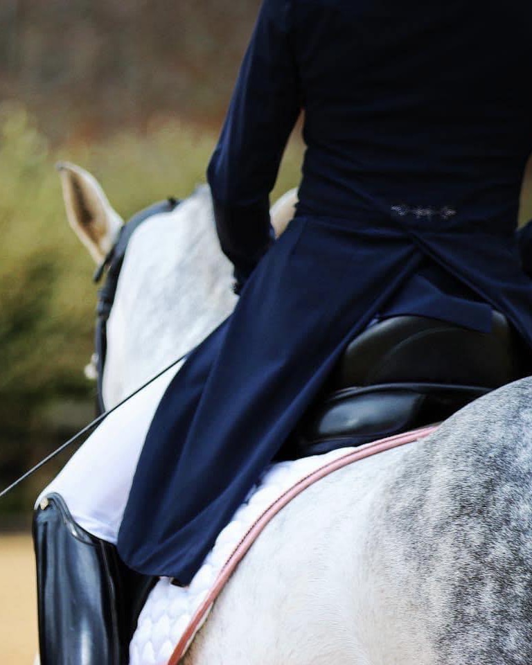 Madison Lareau in a navy shadbelly riding a dappled grey horse at a dressage competition